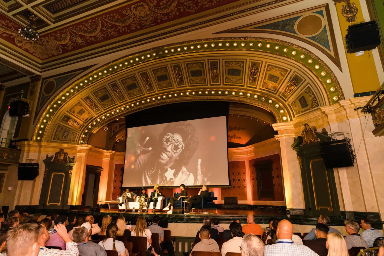 Panel discussion on an ornate theater stage in Cincinnati, with a large screen of Bootsy Collins behind the speakers