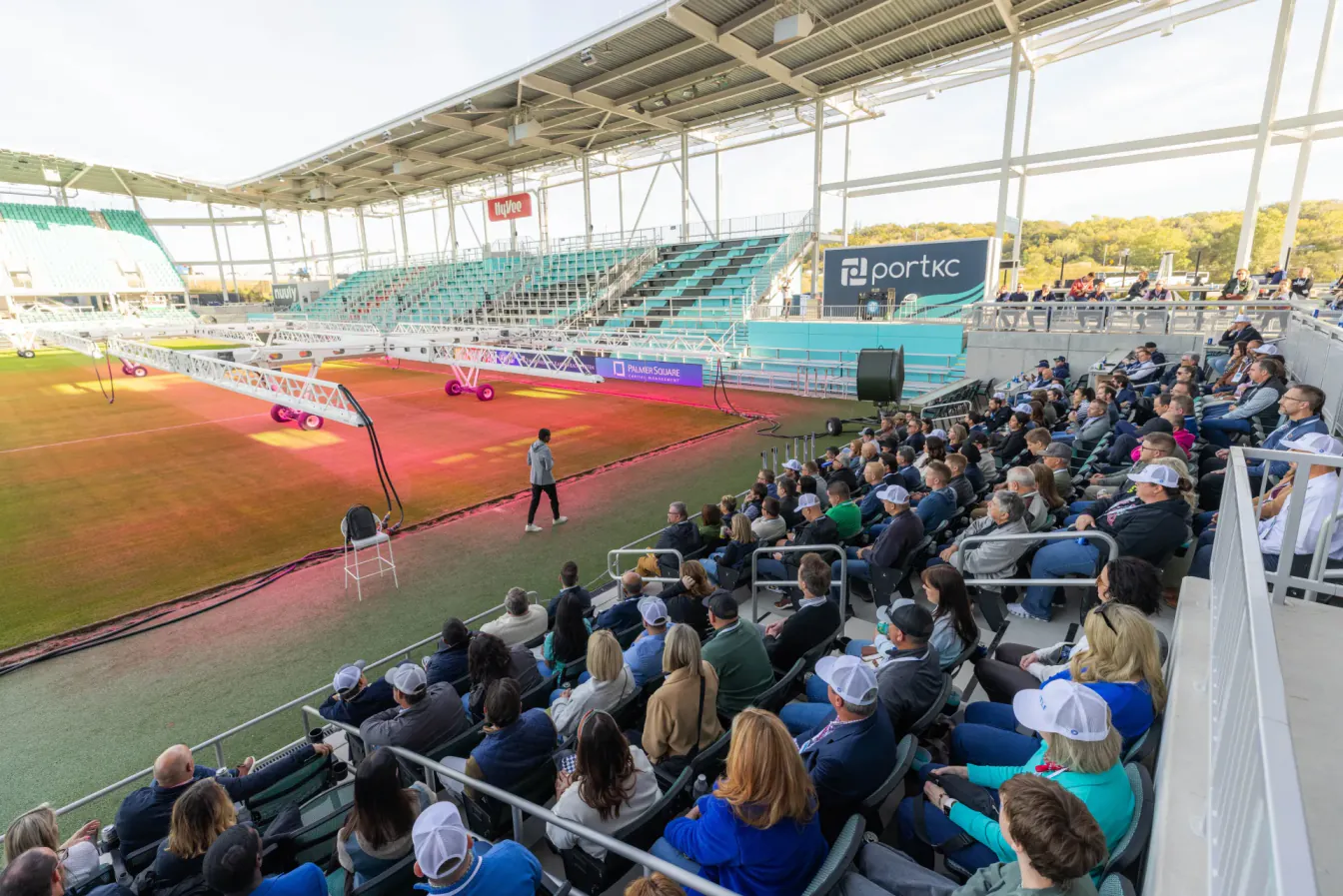 Outdoor session in the stands at portKC, with attendees facing a speaker on the field