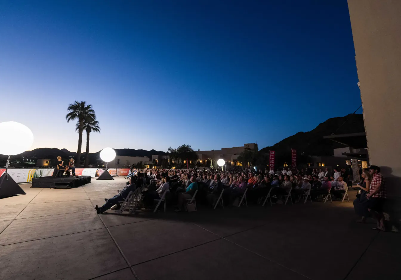 Evening outdoor session in Scottsdale, audience in white chairs under globe lights and Reignite banners